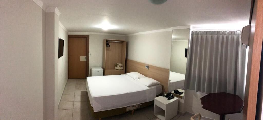 A hotel room with a bed, bedside table, chair, and a small table with a lamp.