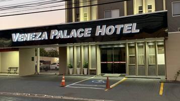 Fachada del Hotel Venezuela Palace con un letrero sobre la entrada, un área de estacionamiento con espacios para discapacitados y un camino de acceso con portones.