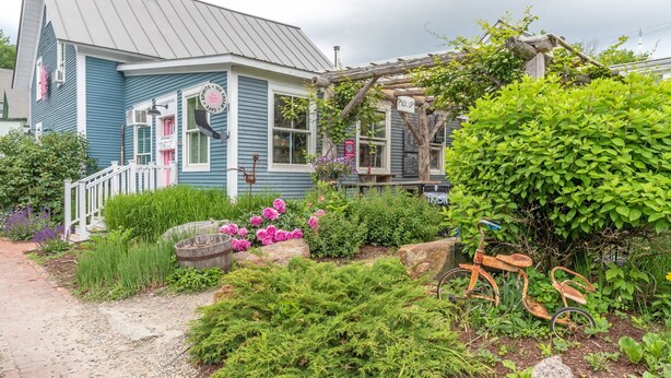 Une maison charmante avec un porche, un jardin fleuri et quelques plantes, et un vélo.