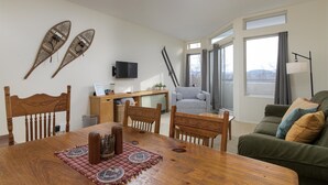 Un salon comprenant une table à manger en bois, des chaises, un canapé gris et un téléviseur fixé au mur.