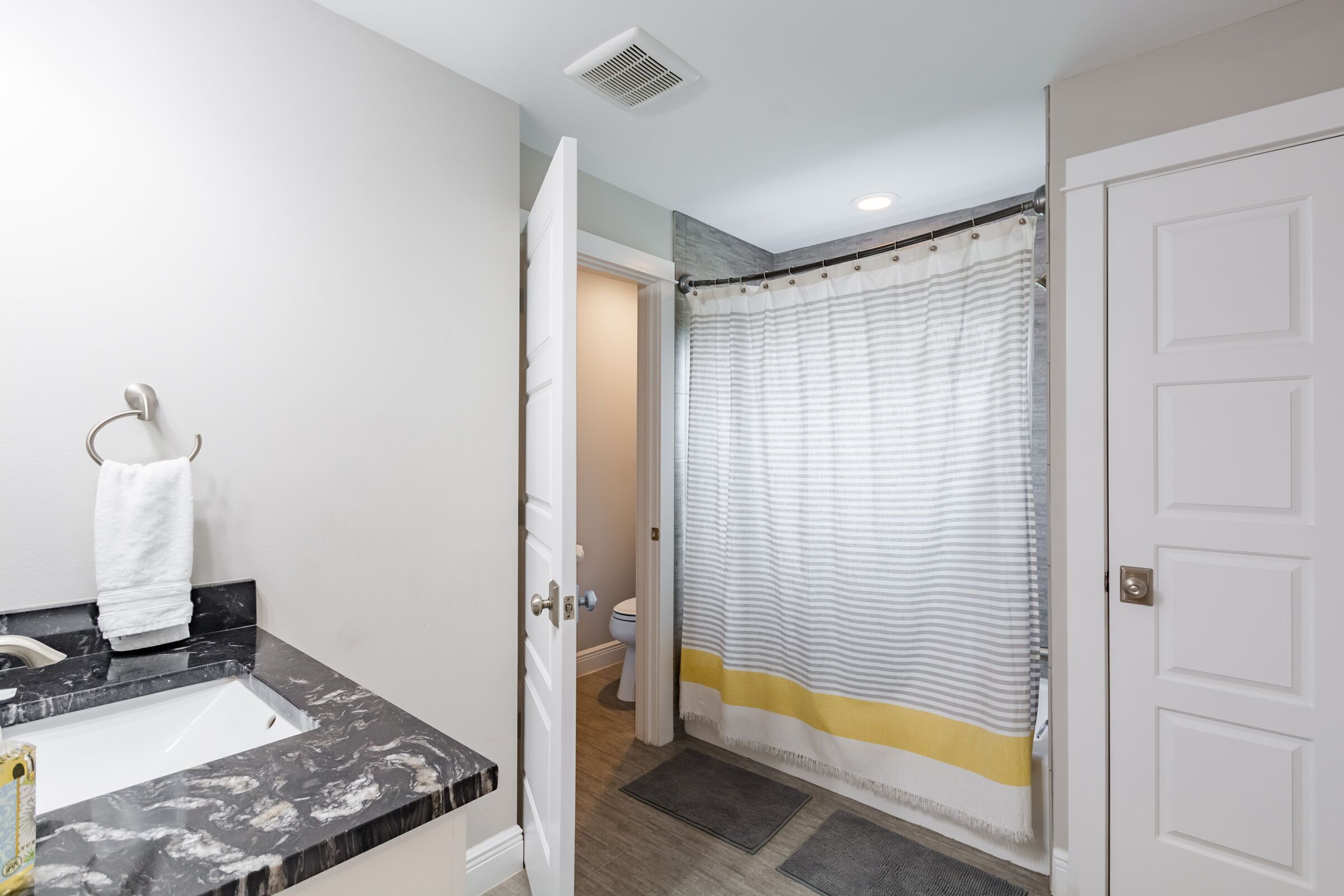Un baño con lavamanos de mármol, toallero, cortina de ducha y puerta que da a otra habitación.