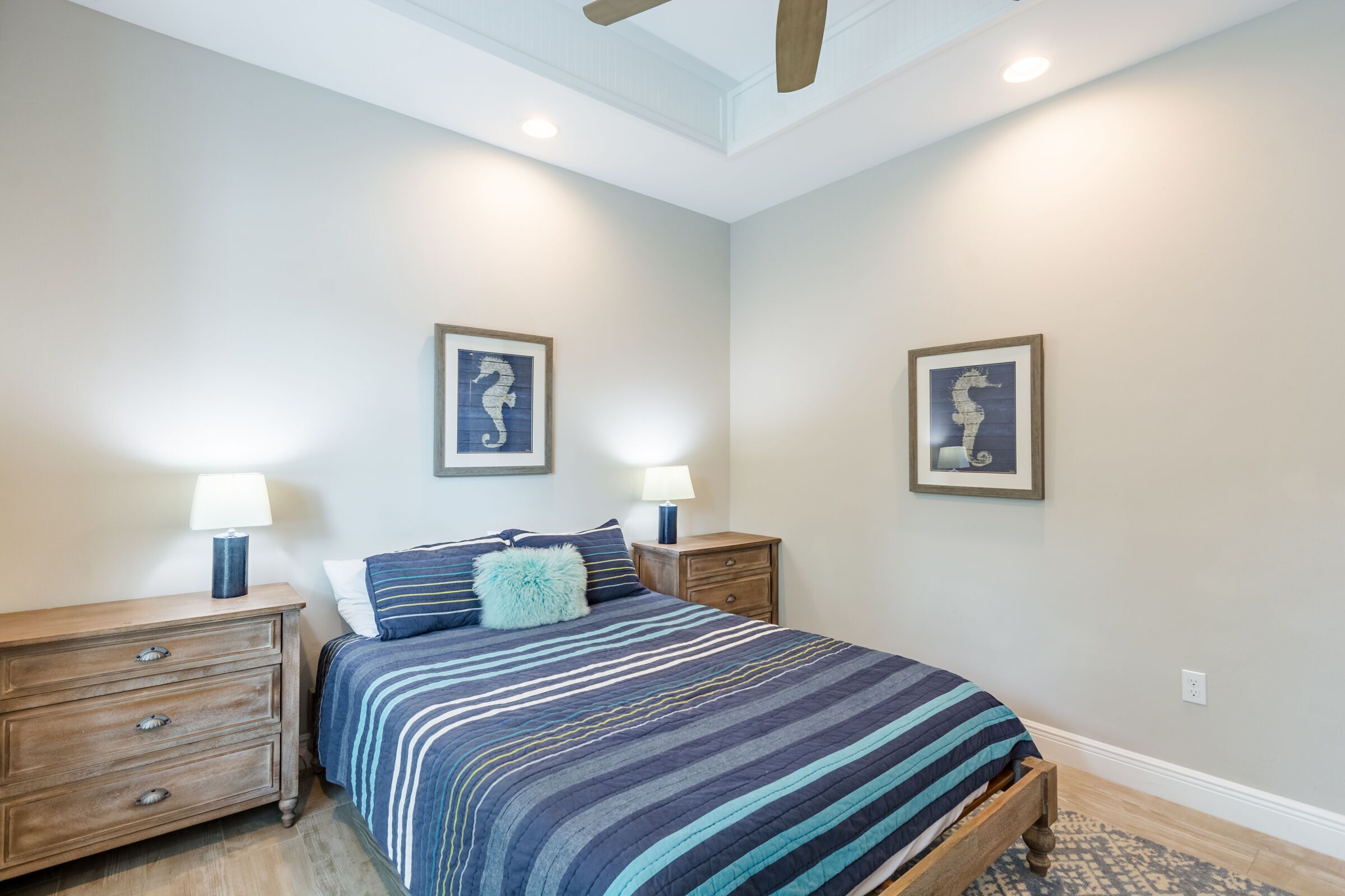 A bedroom with a bed, two nightstands, two lamps, and two framed pictures on the wall.