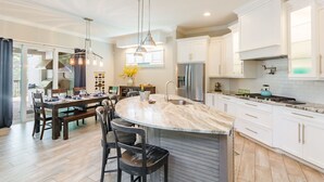 A modern kitchen with white cabinetry, a large island, and a dining area with a table and chairs. - The Seagrape Villa -Family Friendly- Luxury Accommodation in Paradise (Sarasota)