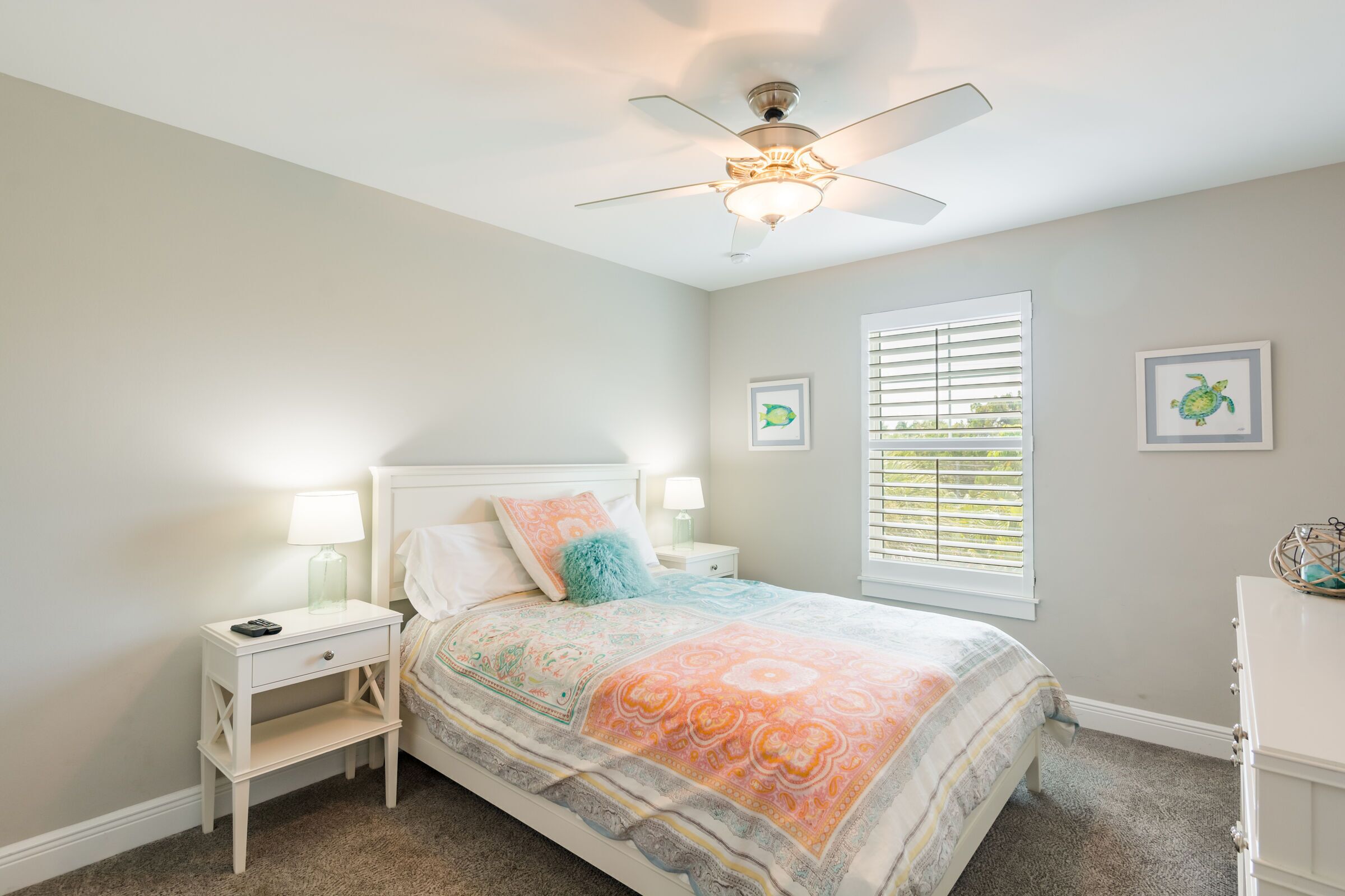 A bedroom with a bed, nightstands, a ceiling fan, a window with blinds, and two framed pictures on the wall.