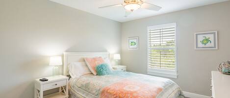 A bedroom with a bed, nightstands, a ceiling fan, a window with blinds, and two framed pictures on the wall.