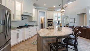 A modern kitchen with white cabinetry, a central island with a sink, a stainless steel refrigerator, and a gas stove. - The Seagrape Villa -Family Friendly- Luxury Accommodation in Paradise (Sarasota)