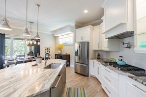 A modern kitchen with a marble island, stainless steel appliances, and pendant lighting.