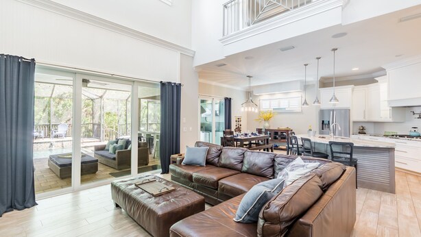 A spacious living room with a large brown leather sofa, a dining area with a kitchen in the background, and a view of a pool through large glass doors. - The Seagrape Villa -Family Friendly- Luxury Accommodation in Paradise (Sarasota)