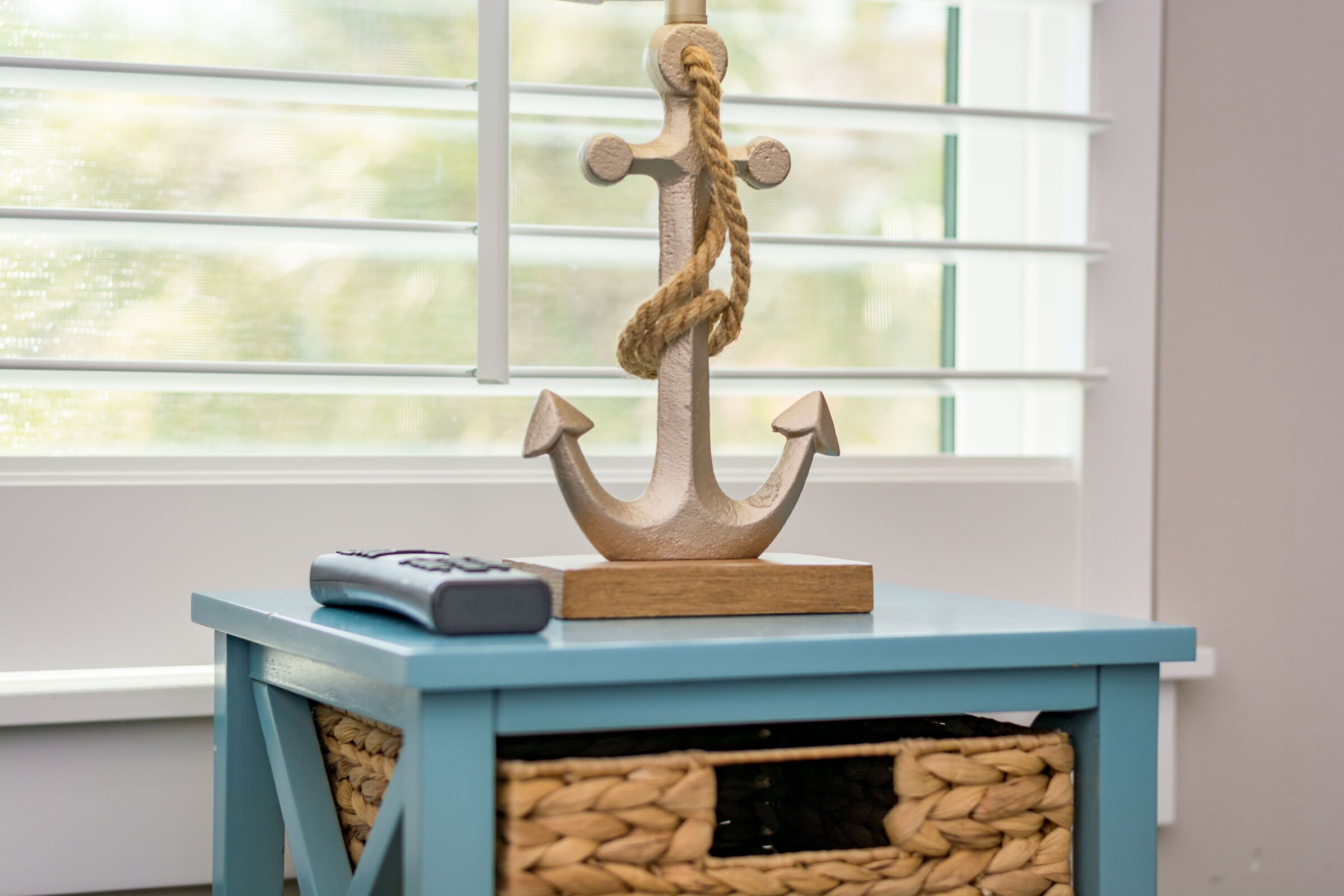 A blue wooden side table with a woven basket and a decorative anchor.