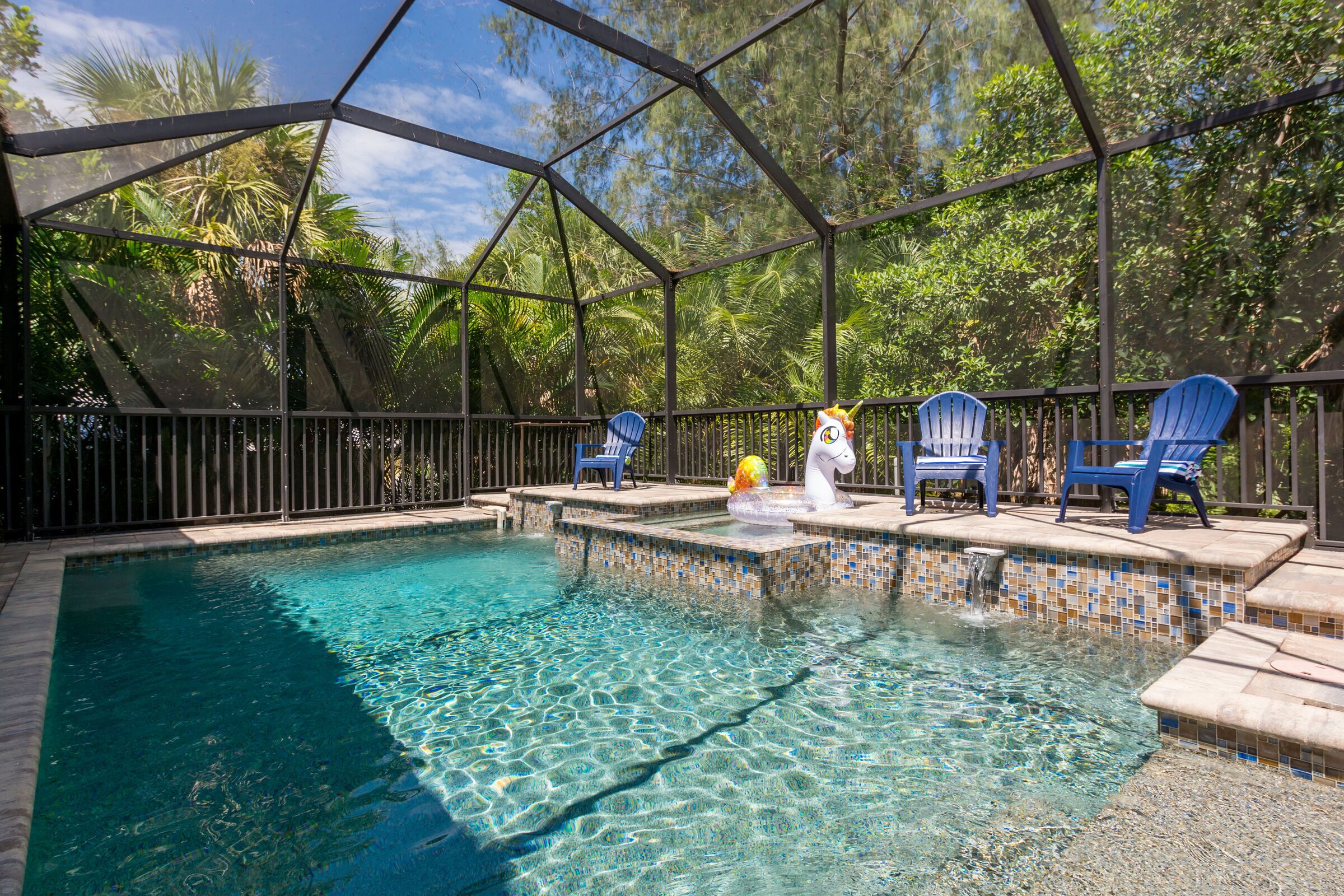 A clear swimming pool with a tiled edge, surrounded by a covered area with blue chairs and a swan decoration.