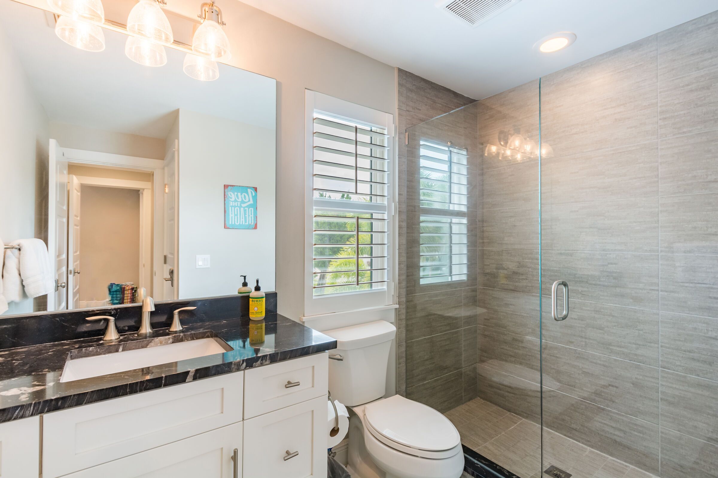 A modern bathroom with a black marble countertop, a white toilet, and a glass shower enclosure.