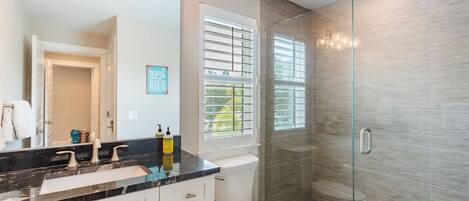 A modern bathroom with a black marble countertop, a white toilet, and a glass shower enclosure.