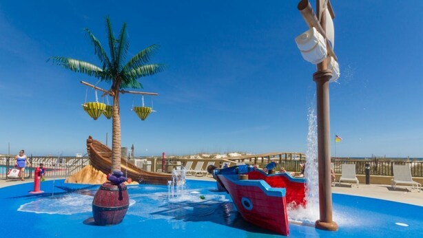 A water play area with a palm tree, a wooden boat, and a water fountain. - Phoenix V Unit 816 (Orange Beach)