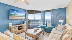 A living room with a television, a wooden coffee table, and a sofa. There is a balcony with a view of the ocean. - Phoenix V Unit 816 (Orange Beach)