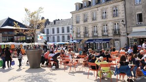 Ein Straßencafé mit Tischen und Stühlen, umgeben von Gebäuden mit Geschäften und Schildern.