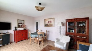 A living room with a television, red dresser, wooden chairs, a white armchair, and a cabinet with glass doors.