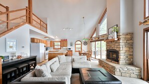 Una zona d'estar àmplia amb un sofà modular gran, una llar de foc i una cuina al fons.