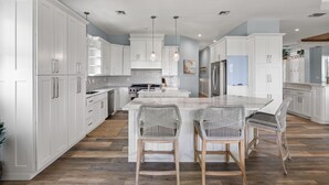 Une cuisine moderne avec des meubles blancs, un îlot central doté de tabourets et des luminaires suspendus.