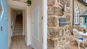 Un muro de piedra con un letrero que dice "1 Chapel Mews", una puerta blanca y una escalera que sube a un piso superior.