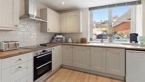 Una cocina moderna con armarios blancos, encimera de madera, horno empotrado, tostadora y ventana con vistas a la calle.