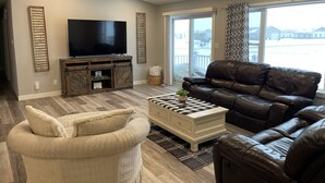 Una sala de estar con un televisor de pantalla plana grande, sofás de cuero, un sillón blanco y una mesa de centro con una planta.
