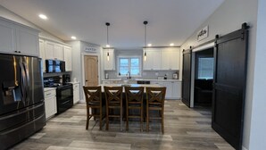 Una cocina moderna con armarios blancos, un refrigerador negro, una mesa de comedor de madera con cuatro sillas y un ventanal que proporciona luz natural.