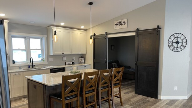 Una cocina moderna con una isla central, sillas de madera, iluminación colgante y una puerta corredera estilo granero.