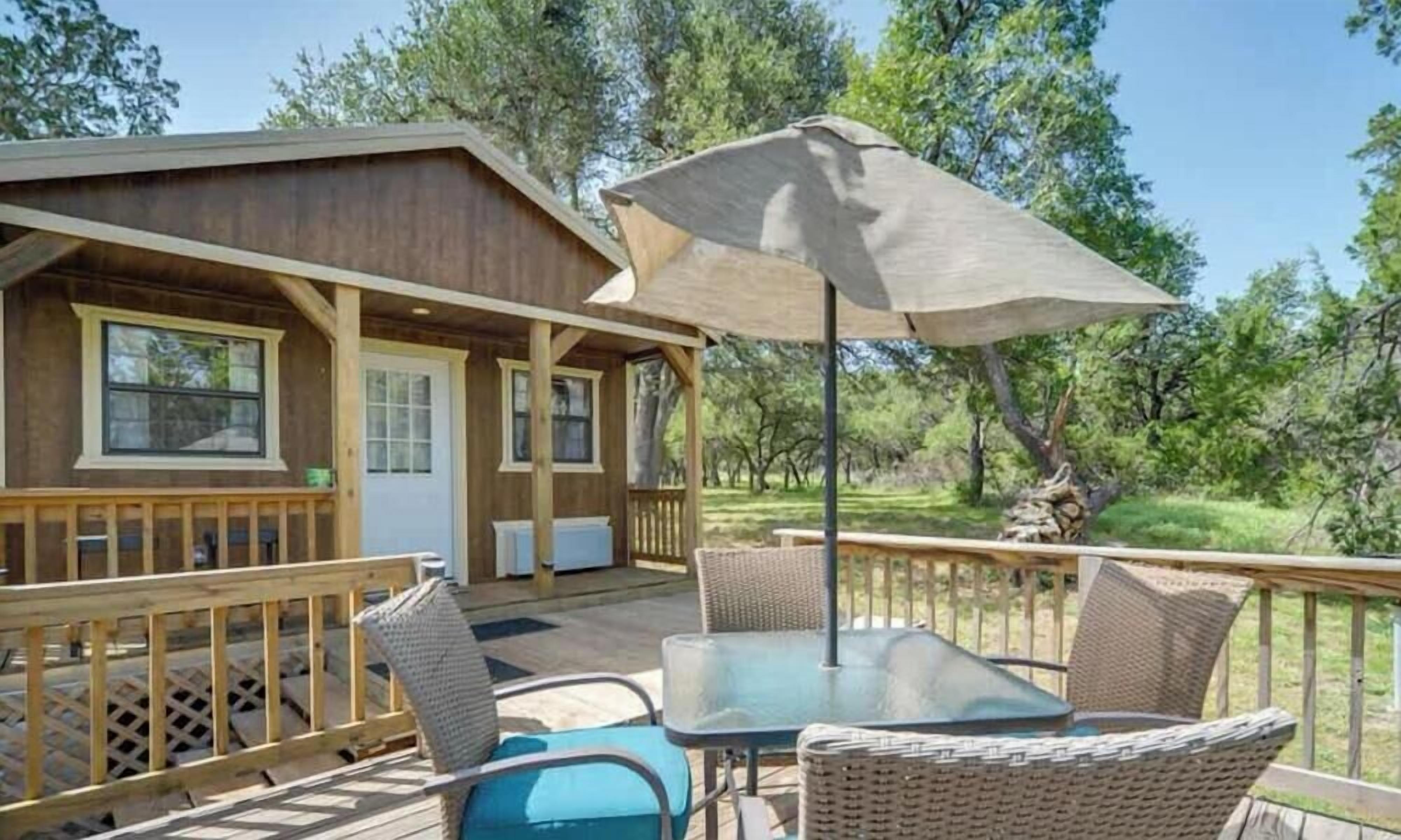 A wooden cabin with a deck, outdoor seating, and a large umbrella.