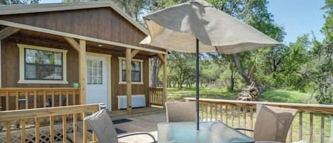 A wooden cabin with a deck, outdoor seating, and a large umbrella.