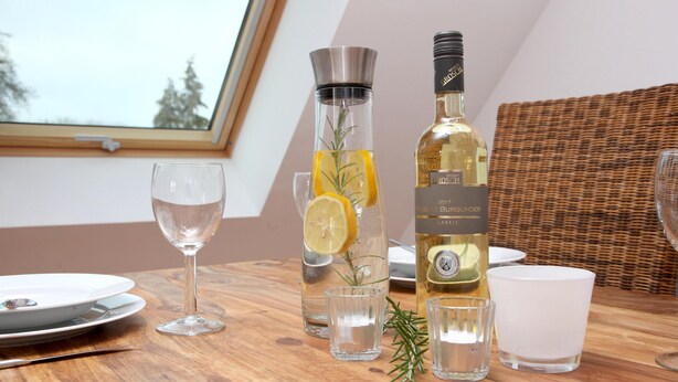 A dining table with a bottle of rosé wine, a glass pitcher with lemon slices, and a glass of water.