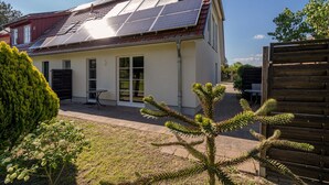Ett hus med solpaneler på taket, en liten uteplats och ett trästaket.