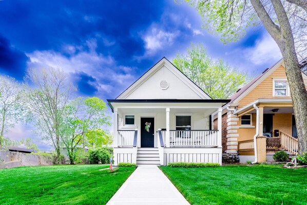 A two-story house with a front porch, a small front yard, and a clear sky.