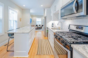 A modern kitchen with white cabinetry, a central island, a stove, and a microwave.