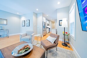 A modern living room with a sofa, a coffee table with a decorative plate, a dining area with a table and chairs, and a kitchen in the background.