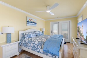Quarto com cama, mesas de cabeceira, ventoinha no teto, janela com persianas e um quadro na parede.