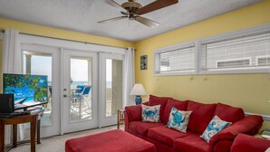 A room with a red sofa, a laptop on a table, and a view of the ocean through a sliding door. - "Waters Edge 427-D" - Oceanfront Condo w/ Community Pool, 2 Bedrooms / 2 Bathrooms (Holden Beach)