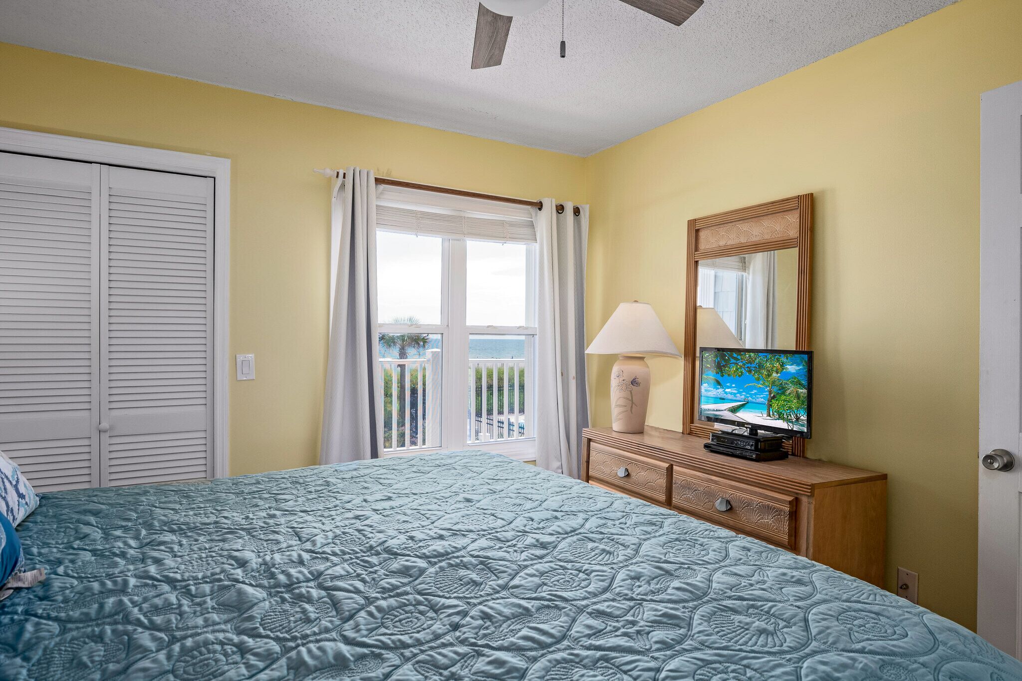 Ein Schlafzimmer mit Bett, Fernseher, Lampe und einem Balkon mit Vorhängen.