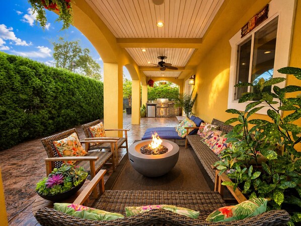 An outdoor patio with wicker furniture, a fire pit, and a kitchen area.