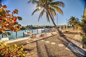 A pool area with lounge chairs and a boat, surrounded by palm trees and a clear sky. - Waterfront 2br/2ba condo w/ boat slip, private ramp & chilled/heated pool (Marathon)