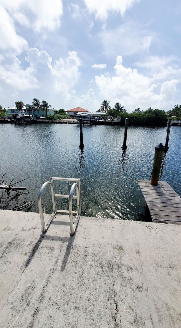 A concrete dock with a metal chair, a calm water body, and a clear sky with clouds. - Waterfront 2br/2ba condo w/ boat slip, private ramp & chilled/heated pool (Marathon)