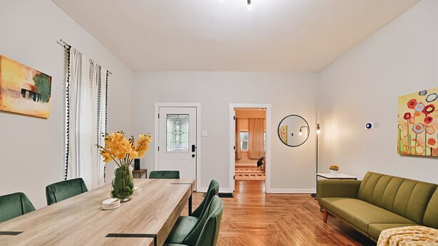 Ett modernt vardagsrum med ett matbord i trä, gröna stolar, en grön soffa och en golvlampa.