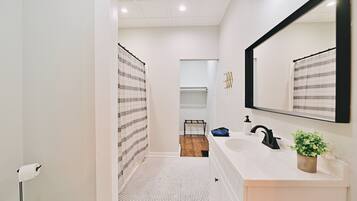 A modern bathroom with a white sink, black faucet, and a large mirror. There is a striped shower curtain and a small plant on the vanity.