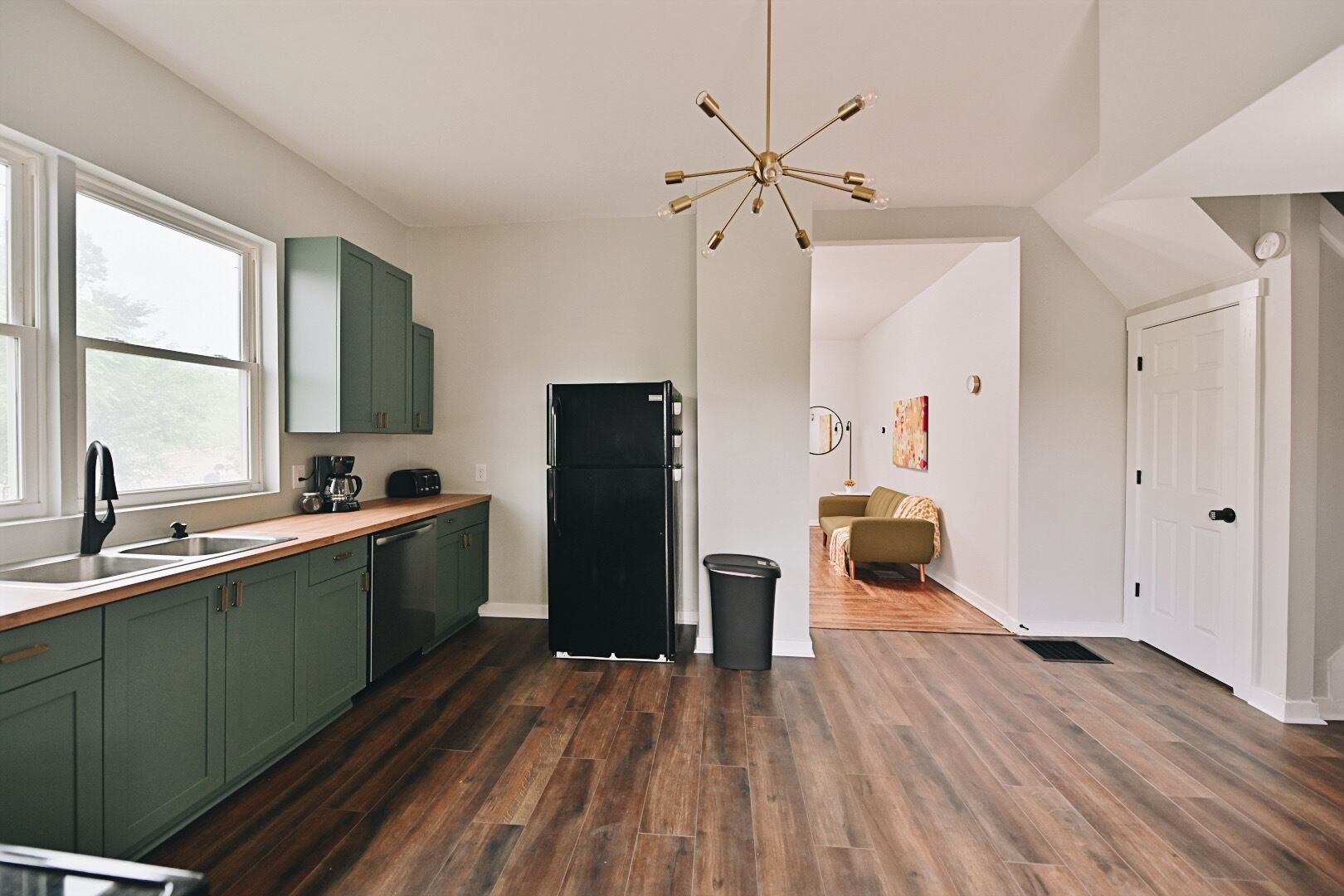 A modern kitchen with green cabinets, a black refrigerator, and a wooden floor.