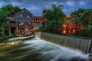 A historic mill with a water wheel, wooden buildings, and a pond.