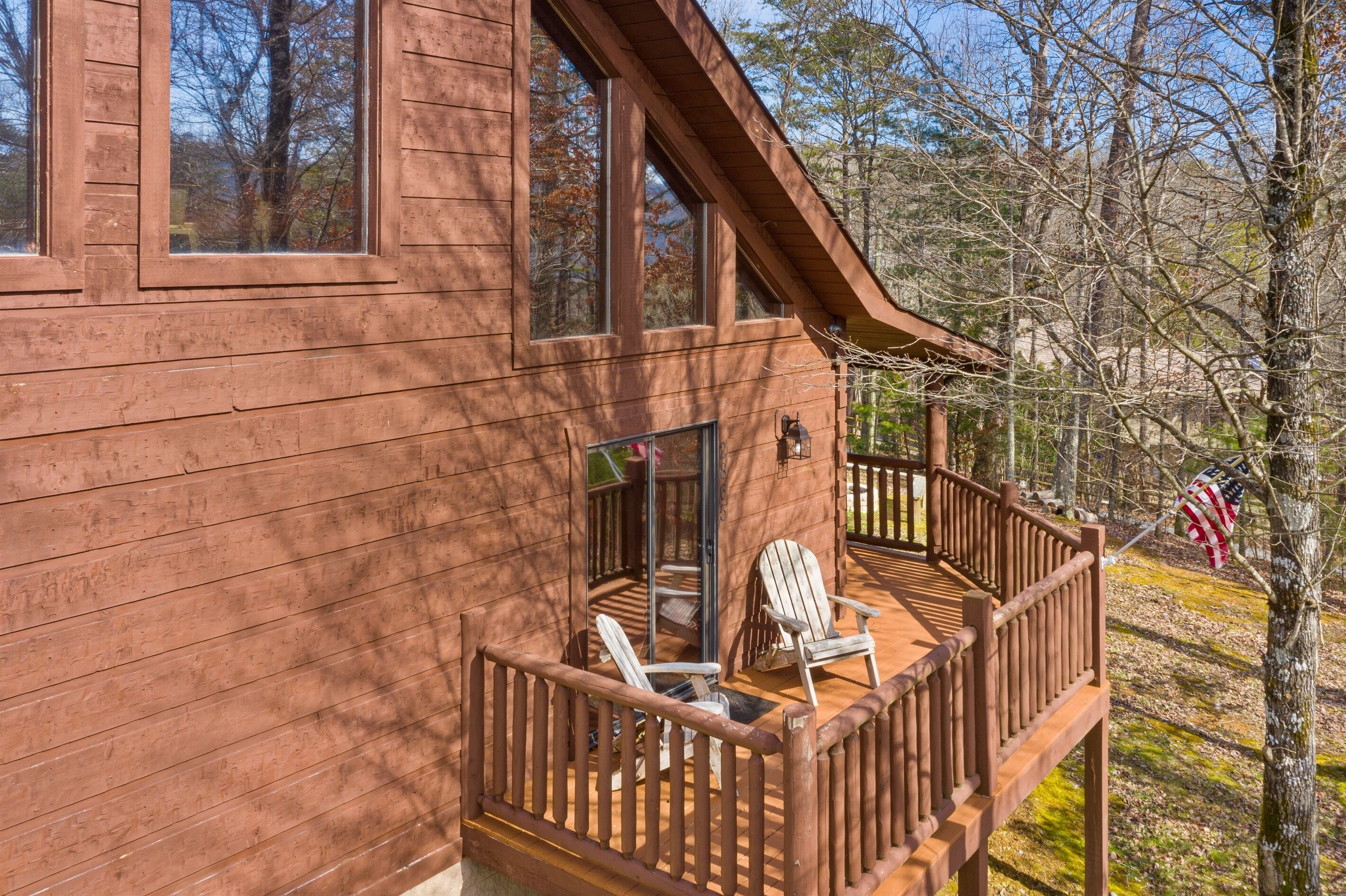 Een houten chalet met een terras, twee Adirondack-stoelen en een Amerikaanse vlag.