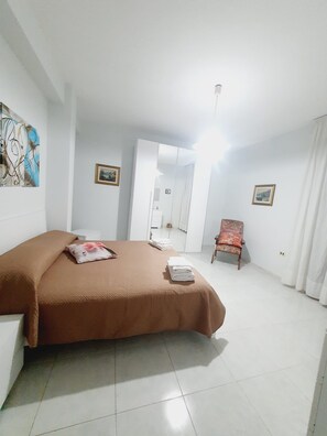 Une chambre d’hôtel avec un lit, une chaise, un tableau au mur et une porte donnant sur une autre pièce.