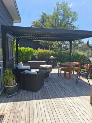 A covered outdoor patio with wicker furniture, a hot tub, and a wooden table. - Beks Retreat,  100 metres walk to Estuary, (Mangawhai Heads)