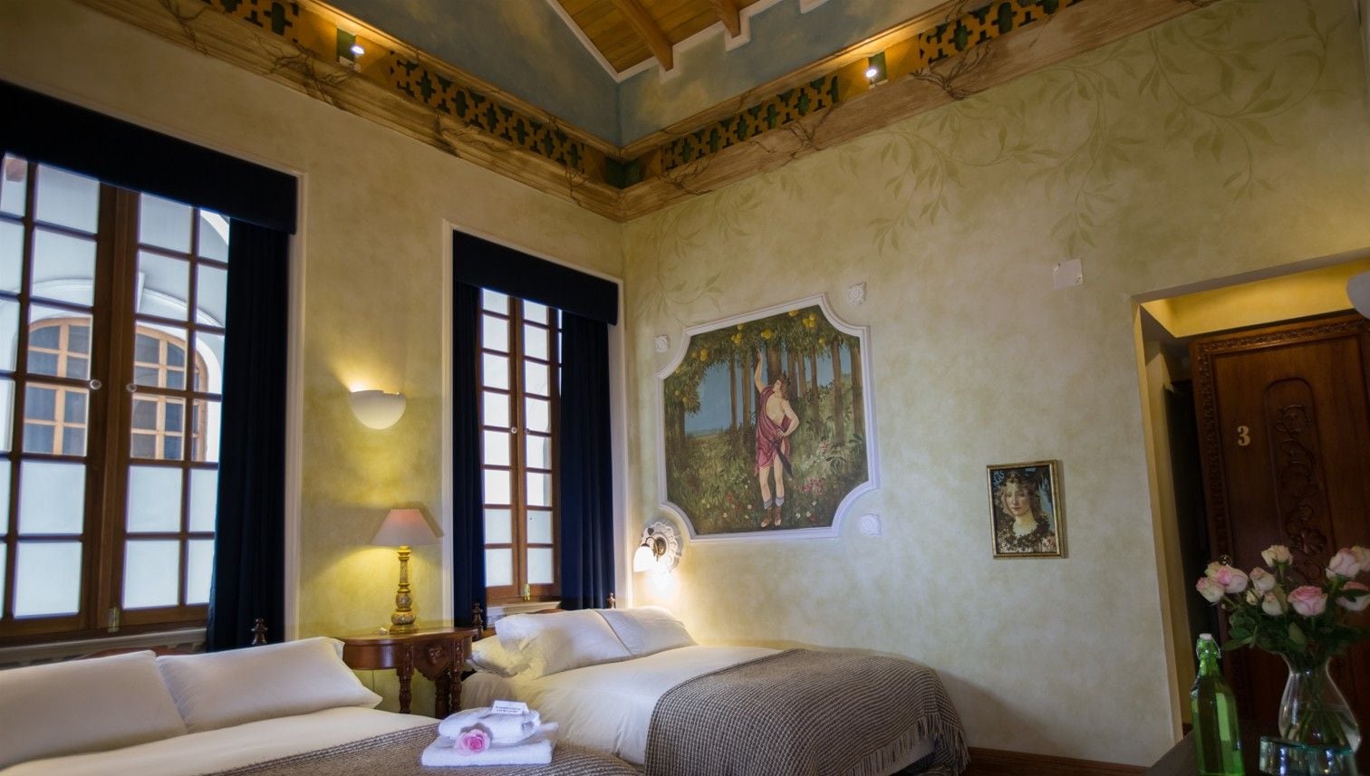 A hotel room with a bed, a nightstand, a lamp, a painting, and a door.