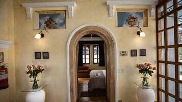 A hallway with an arched doorway leading to a bedroom, flanked by two vases of flowers and framed pictures on the walls.