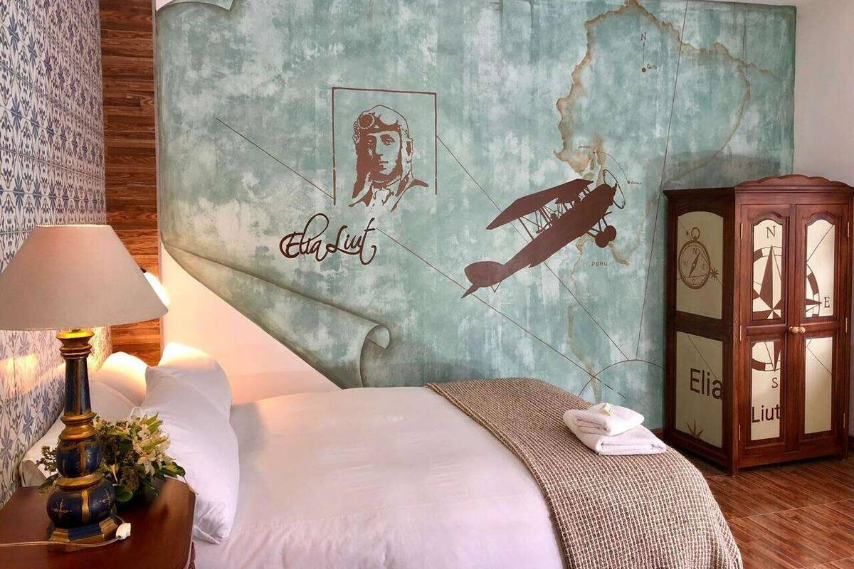 A bedroom with a large bed, a nightstand with a lamp, a map mural on the wall, and a wooden cabinet.